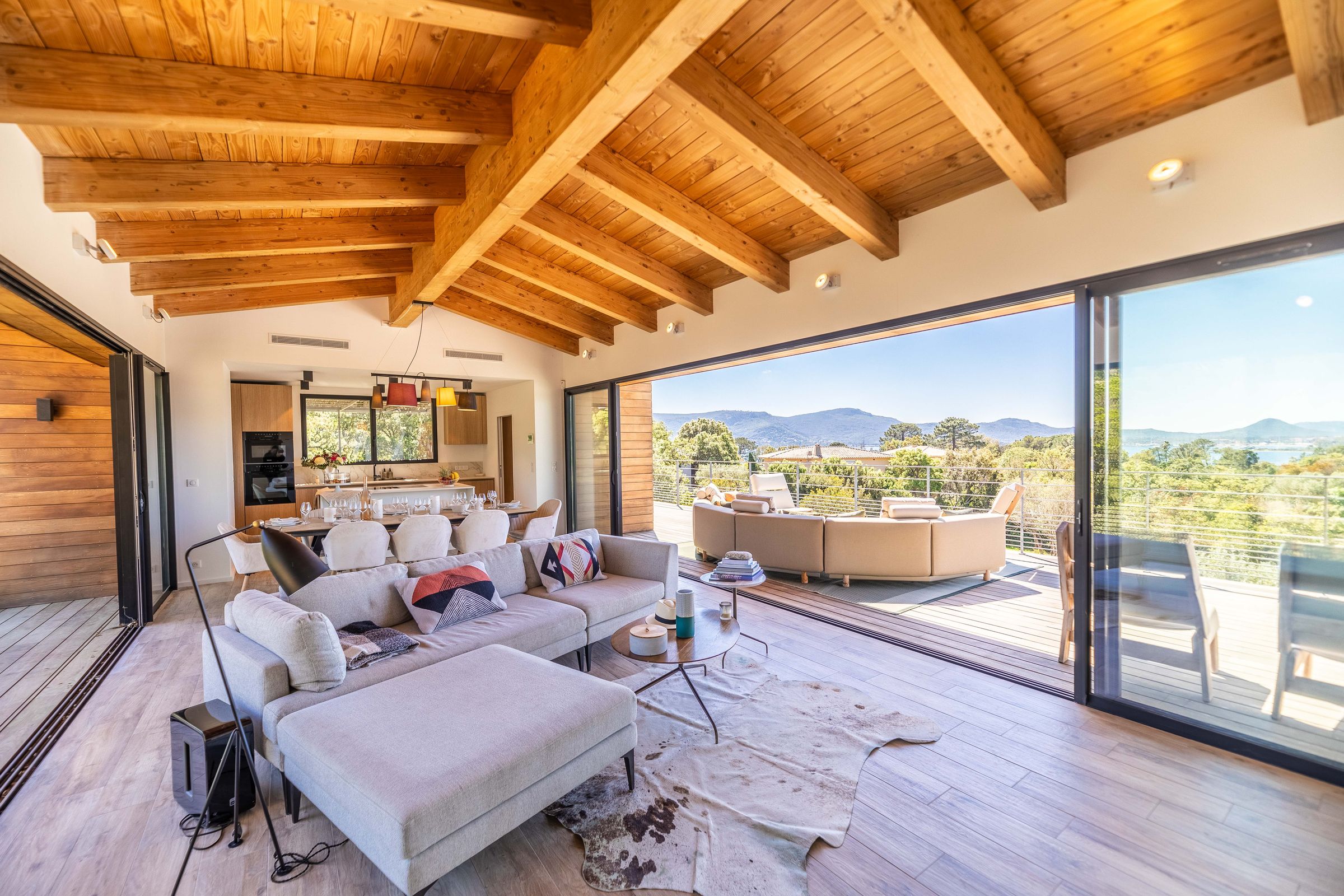 Living room under the exposed timber ceiling, open to the terrace and the sea